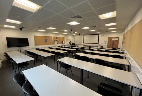 Dalhousie 2S13 - rows of tables and chairs with a white screen at the front of the room. A flat screen tv on a mobile stand on the floor 