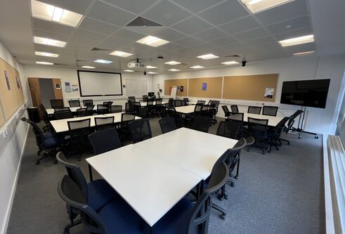 Dalhousie 2S14 - several tables set in squares with chairs. A mobile tv screen on the floor and white screen at front of room