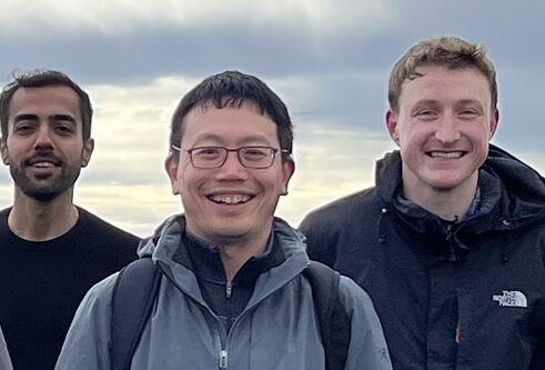 Three men standing next to one another outside on an overcast day
