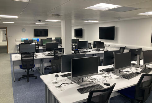 IT Suite in Tower basement showing several desks in rows with computers, mouse and keyboards