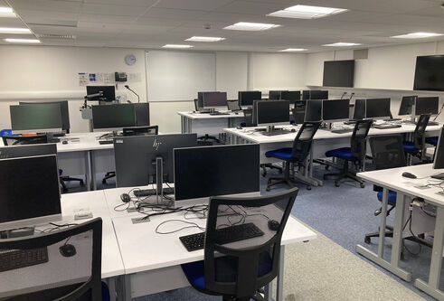 IT Suite in Tower Basement, Suite E showing several desks in a row with computer screens, keyboards and mouse