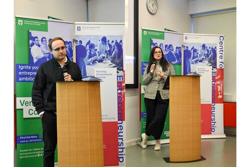A male and female stand at a podium, talking to the room.