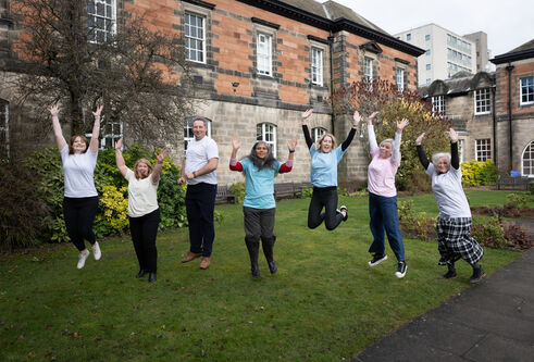 Members of the Playful research group jumping in the air with their hands above their heads set in the Geddes Quadrangle