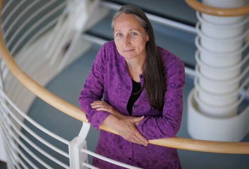 Kate Storey stands in a stairwell with her arms crossed leaning against the bannister, looking up.