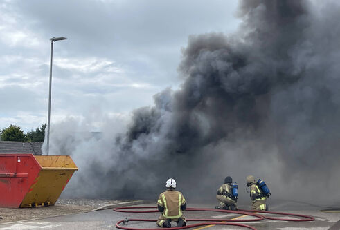 Three fire fighters sit with water houses outside a burning testing facility for training purposes