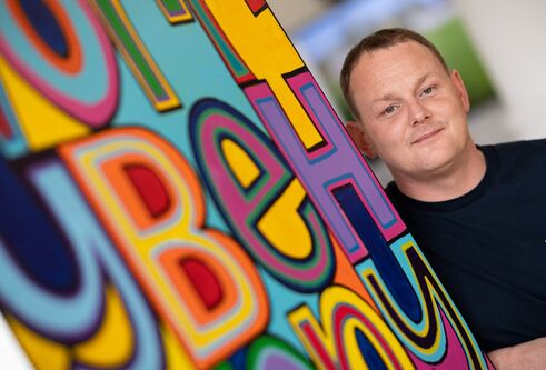 Euan Rutter stood in front of colourful artwork 
