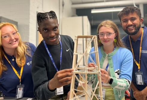 Two Dundee students and two secondary school pupils pose around a mock-up rocket landing tower build, made out of wood