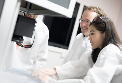 Three people standing over machinery in a lab