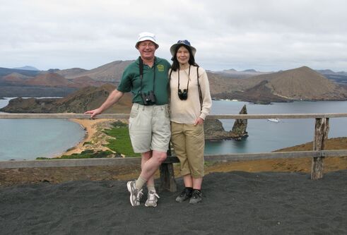 Tricia and Philip stood in front of water and mountain view behind