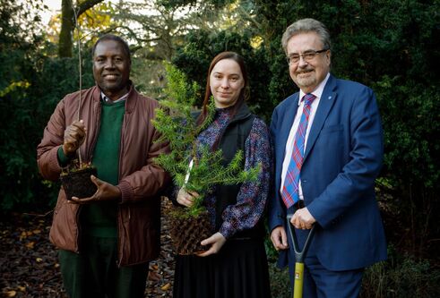 Principle stead with a spade and two other people holding small trees. 
