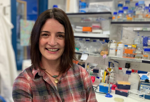 Leeanne McGurk in a lab with rows of bottles on shelves behind 