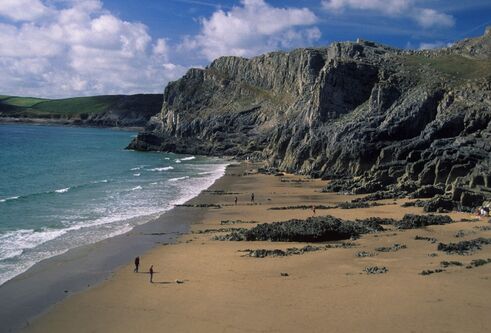 A coastline with a big sandy beach, ocean and rocky cliffs.
