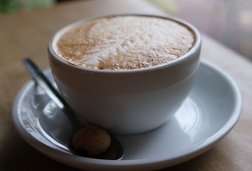 A photograph of a cup of coffee on a saucer with a teaspoon on a wooden table.
