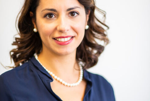 Woman with brown hair wearing a blue shirt with a necklace is smilling