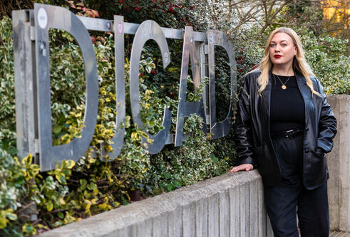 Wonan with blonde hair wearing black stood outside next to the DJCAD sign