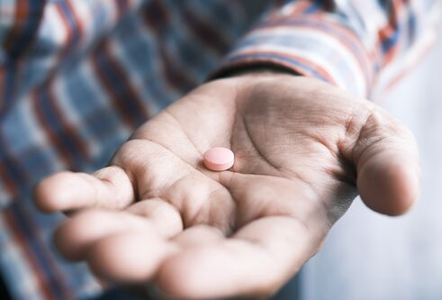 A man's hand outstretched with a pill in his palm