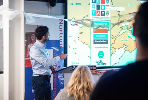 A man stands in front of a screen presenting to a room of people.