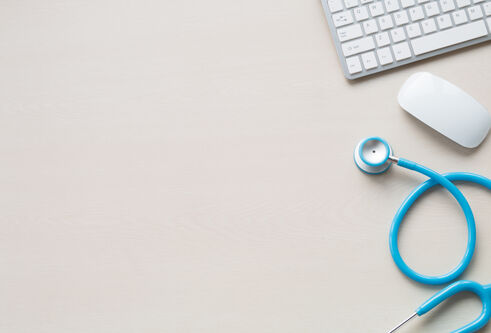 An aerial view of a desk with a stethoscope, mouse and keyboard on the right hand side