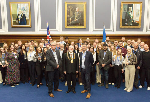 A large group of people dressed smartly stand in front of three large portraits.