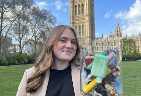 Woman holding a jar filled with discarded disposable vapes, standing outside Westminster