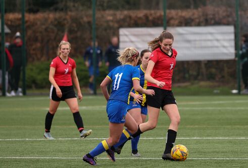 action shot of women playing football. Player with red has ball and player with blue is going in to tackle