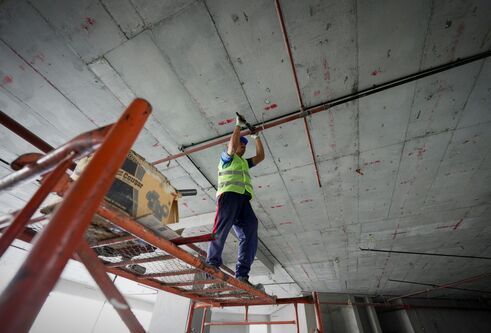 A construction worker on a cherry picker works on a concrete roof