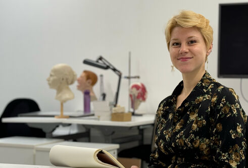 Cydney Davidson sits at a desk, smiling, with a sketch notebook placed in front of her