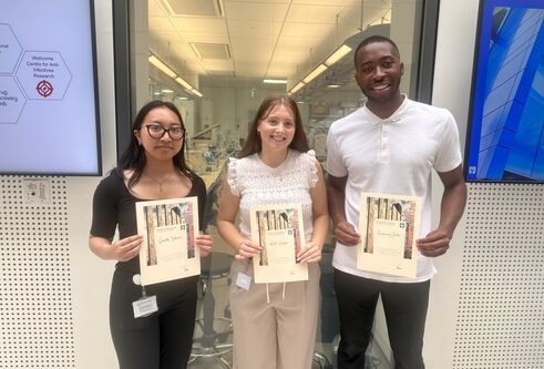 Three people stood next to each other smiling and holding certificates.