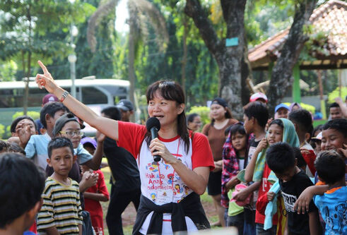 Lina speaking into a microphone surrounded by children