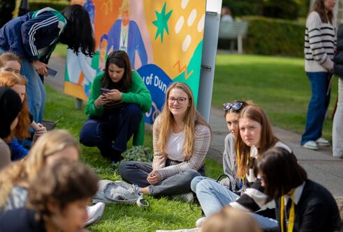 A cheerful group of young adults sitting on the grass, sharing laughter and stories in a vibrant outdoor environment.