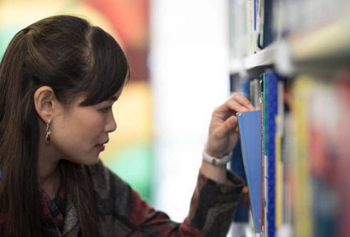 A woman sorts through a book shelf in a library 
