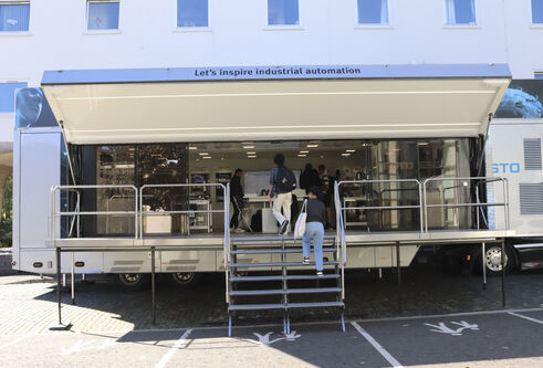 An open sided trailer with people walking up the steps and entering. The words "Lets inspire industrial automation" are above the entrance.