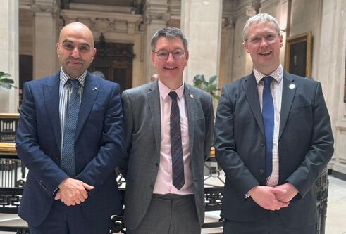 three men standing in a line wearing suits and ties and smiling at the camera
