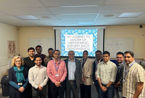 A group of people stand in front of a presentation screen, which says "My journey to master of orthopaedic surgery (MCH orthopaedics)