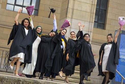 A group of women wearing academic robes at the University of Dundee's Winter Graduation raising their hands and bouquets of flowers as they cheer