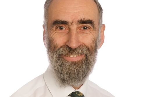 head and shoulders image of man in a white shirt and tie with grey beard, looking and smiling at camera. 