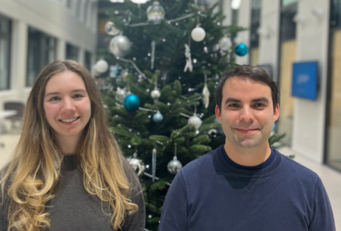 Two people smiling in front of a Christmas tree