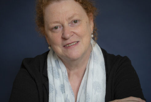 Woman with red hair wearing a light coloured scarf and dark top smiling with her arms folded