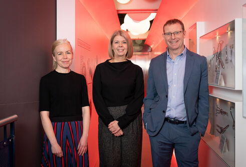 Dr Morag Martin, Dr Pamela Duke and Ronnie Palin standing, smiling, in an orange-lit corridor