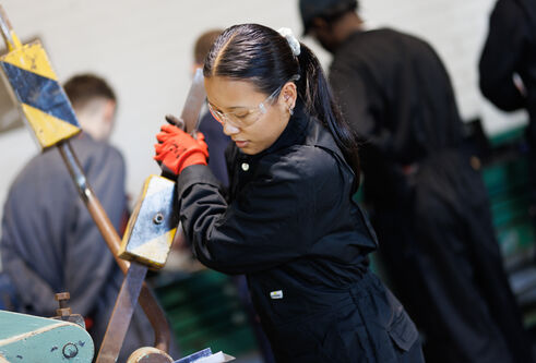 A female student in a boiler suit and gloves operates a piece of industrial equipment