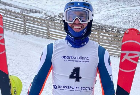 A man wearing white and blue ski suit holding a ski in each hand.