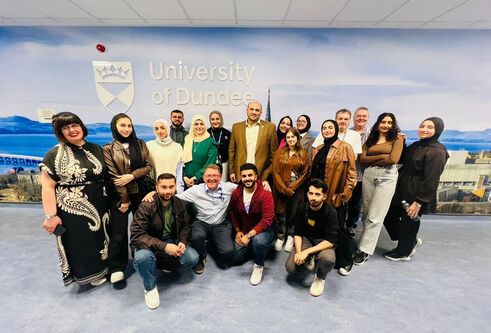 A group of students and a lecturer standing in front of a University of Dundee poster