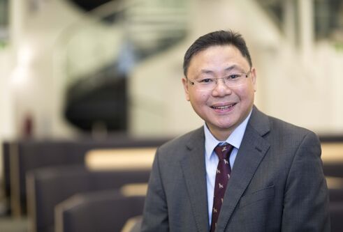 man wearing glasses and suit looking and smiling at camera. background is blurred