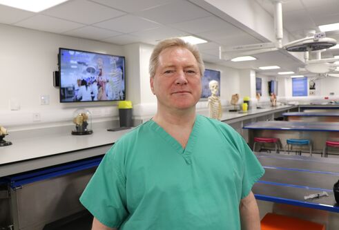 man wearing hospital scrubs looking at camera and smiling. Behind him are tv screens on the walls with medical image on them