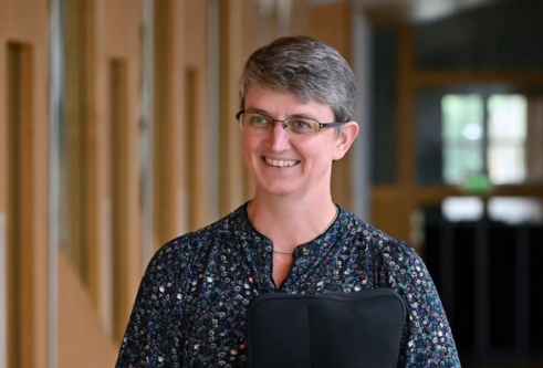 A woman in a dark blouse with short hair smiling in walking down a hallway