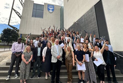 The University of Dundee's Access Summer School Class of 2024 stand on the steps of the University's Dalhousie Building, raising their certificates in the air in joy