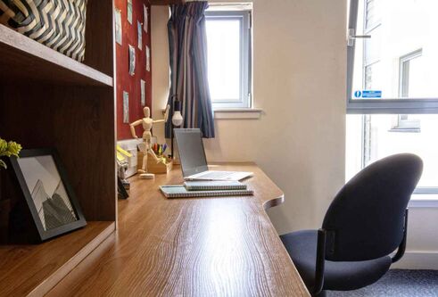 A close up of a study area in a student room with a laptop on the desk and shelving