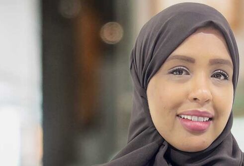 A person wearing a head scarf is looking forward, smiling.