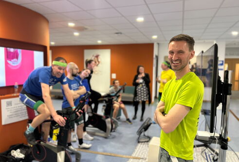 People on the left are using stationary bikes, a person stands to the left wearing a bright green t-shirt, laughing.