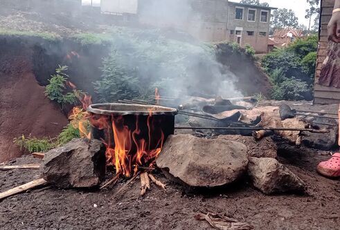 Open fire with cooking pot, and person standing nearby in orange trousers